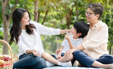 Happy Asian family have come picnic in park together for summer holidays. Boy enjoy travel with their mother and grandma in the park Beautiful nature. Concept Health care insurance