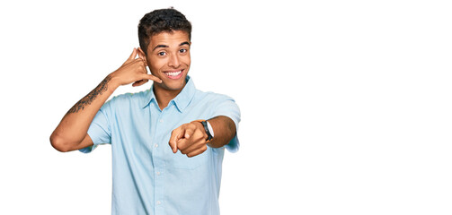 Young handsome african american man wearing casual clothes smiling doing talking on the telephone gesture and pointing to you. call me.