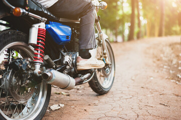 The motorcycle is driving on a dirt road in the forest. A young man driving a motorcycle on a...