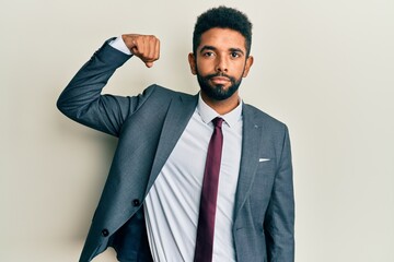 Handsome hispanic man with beard wearing business suit and tie strong person showing arm muscle, confident and proud of power