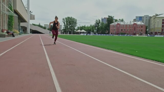 Brunette woman runner running on racetrack. Sport woman jogging on athletics track outdoor. Full length shot