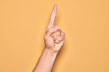 Hand of caucasian young man showing fingers over isolated yellow background counting number one using index finger, showing idea and understanding