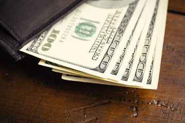 Leather wallet full of money on wooden table - one hundred US banknotes with president Franklin portrait. Cash of hundred dollar bills, paper currency background.