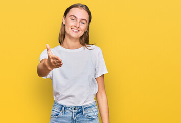 Beautiful young blonde woman wearing casual white t shirt smiling friendly offering handshake as greeting and welcoming. successful business.