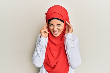 Young beautiful hispanic girl wearing traditional islamic hijab scarf covering ears with fingers with annoyed expression for the noise of loud music. deaf concept.