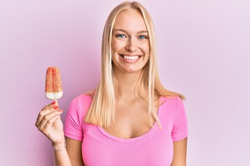 Young blonde girl holding ice cream looking positive and happy standing and smiling with a confident smile showing teeth