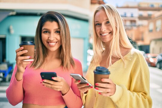 Two beautiful and young girl friends together having fun at the city using smartphone