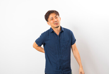 Middle age Asian man suffering from back pain standing on white wall.