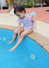 Asian little girl sitting happily at swimming pool outdoors, Thailand.