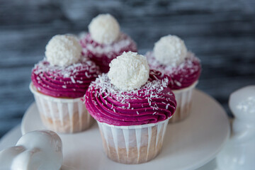 Four delicious cupcake with violet cream decorated with balls topped with coconut crumbs