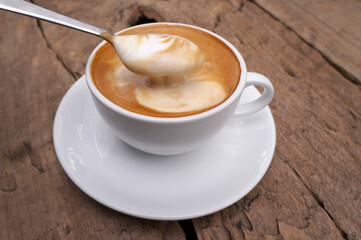 Morning coffee, milk foam in a cup, a soft latte texture that melts. Coffee in a white mug placed on a wooden table