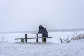 A girl at a table on a bench by the river against the background of a winter landscape during a...