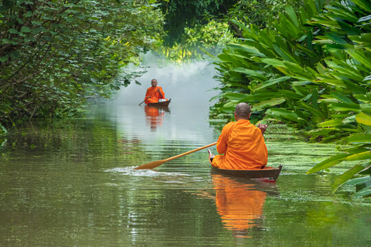 Monks rowing alms on the canal in the morning Through a tree tunnel In the water there is a reflection,The culture tradition Buddhist monk of making merit .