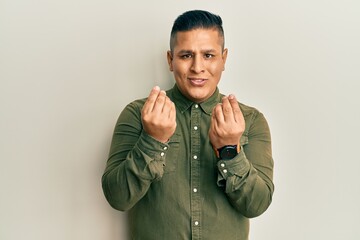 Young latin man wearing casual clothes doing money gesture with hands, asking for salary payment,...