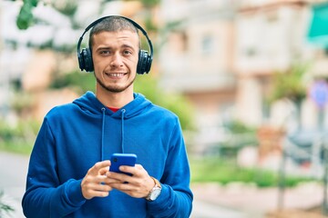 Young hispanic man smiling happy using smartphone and headphones at the city.