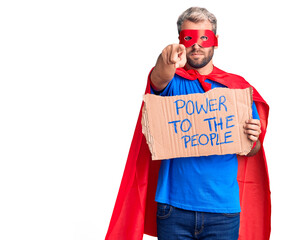 Young blond man wearing super hero custome holding power to the people cardboard banner pointing...