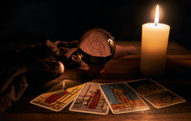 concept of fortune-telling wooden table and white candle with a crystal ball and tarot cards on...