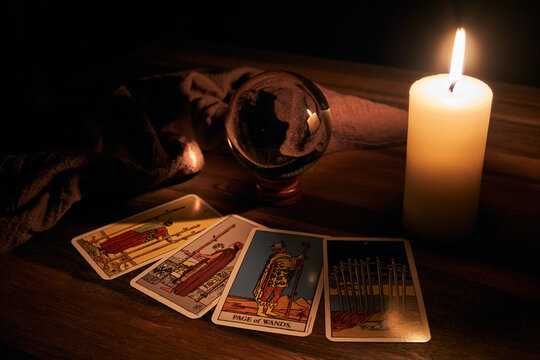 concept of fortune-telling wooden table and white candle with a crystal ball and tarot cards on dark background    