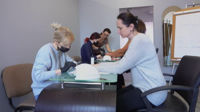 Two manicure masters in black masks take part in retraining courses under the guidance of a teacher
