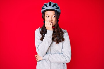 Young beautiful chinese girl wearing bike helmet looking stressed and nervous with hands on mouth biting nails. anxiety problem.