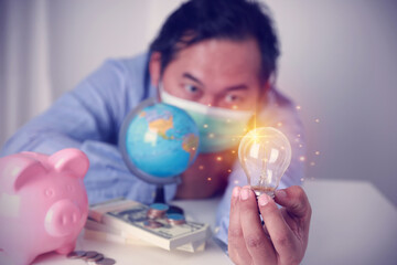 Businessman wearing a mask holding a lightbulb with a pink piggy bank, money,