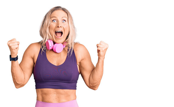 Middle age fit blonde woman wearing gym clothes and using headphones celebrating surprised and amazed for success with arms raised and open eyes. winner concept.