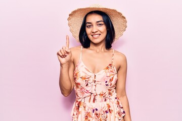 Young beautiful latin woman wearing summer hat smiling with an idea or question pointing finger up with happy face, number one