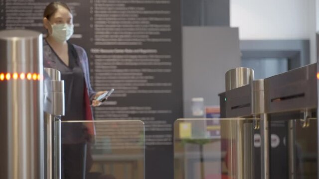 Asian woman wearing surgical mask walks to a shop entrance and uses her phone to scan the entrance QR code to open the gate at a shop 