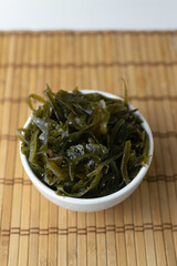 Fresh seaweed in a white bowl on a bamboo mat. Vegetarian food concept. Healthy eating. Vertical orientation.