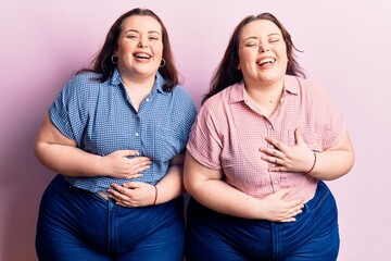 Young plus size twins wearing casual clothes smiling and laughing hard out loud because funny crazy joke with hands on body.