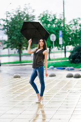 Portrait of a happy woman wearing jeans under an umbrella smiling in the street in a rainy day
