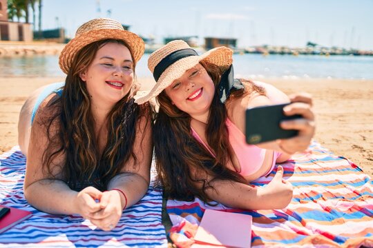 Two plus size overweight sisters twins women happy taking a selfie picture at the beach on summer holidays