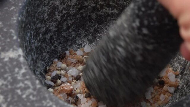 Super close-up of pestle crushing and mixing salt and peppers in the grey stone mortar
