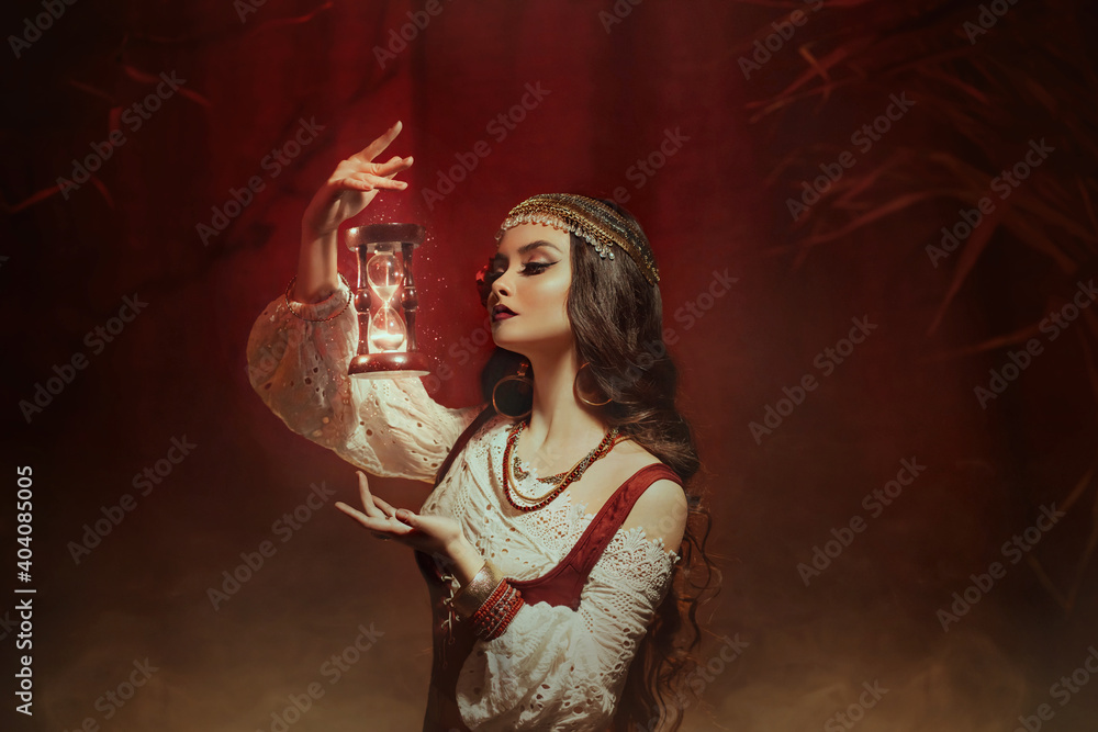 Wall mural Fantasy woman creates magic. Gypsy girl witch holding magical hourglass in hands. Photo levitation. Time control youth concept. Spiritual lady looks, reads future. Fairy tale Image of Fortune Teller