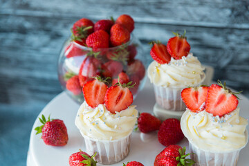 Delicious cupcakes with white cream decorated with strawberries on a gray background.