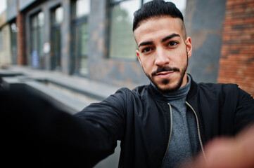 Naklejka premium Portrait of stylish arab beard man wear grey turtleneck and black jaket. Arabian model guy make selfie by camera.