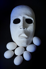 A white scary theater mask lies next to the chicken eggs