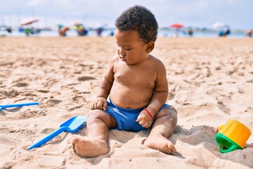 Adorable african american toddler playing with toys sitting on the sand at the beach.