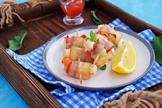 Hot appetizer, shrimp with cream cheese and asparagus beans, wrapped in bacon, on wooden skewers on a ceramic plate. Seafood recipes.
