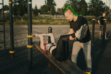 The man the trainer observes the girl performing the exercise on the press of the urban sports ground on an inclined bench.