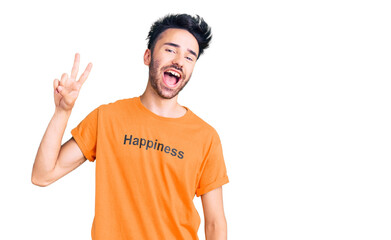 Young hispanic man wearing t shirt with happiness word message smiling looking to the camera showing fingers doing victory sign. number two.