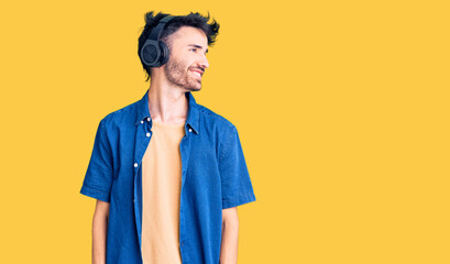Young hispanic man listening to music using headphones looking away to side with smile on face, natural expression. laughing confident.