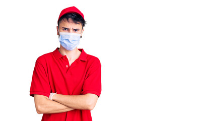 Young hispanic man wearing delivery uniform and medical mask skeptic and nervous, disapproving expression on face with crossed arms. negative person.