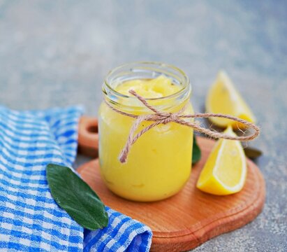 Lemon curd, a sweet fruity custard in a glass jar on a gray concrete background. Cream recipes.