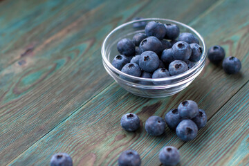 A small glass bowl of ripe blueberries on a blue wooden table copy space.