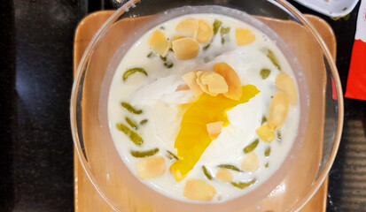 Top view of coconut milk ice cream with peanut, sliced jackfruit and Lod Chong in glass bowl. Flat lay of Thai dessert food on table. 