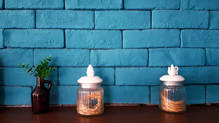 Glass bottle or jug with flower dry inside and brown glass bottle and fake ornamental plant tree on wooden shelf with green pastel brick wall for background. Object decorative and loft style design pa