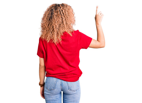 Young blonde woman with curly hair wearing casual red tshirt posing backwards pointing ahead with finger hand
