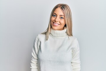 Beautiful blonde woman wearing casual turtleneck sweater with a happy and cool smile on face. lucky person.