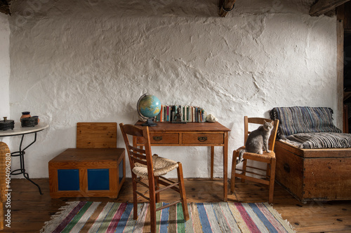 Fototapete Front View Of Vintage Room Interior In Traditional Village Country House Old Handmade Furniture School Desk Wooden Chairs Craft Chest On Stucco Wall Background Georgetsamakdas